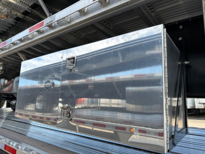 Flatbed trailer side storage box mounted under the flatbed, with polished aluminum diamond-plate door and latch hardware.