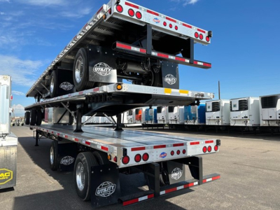 Utility flatbed trailer stack with car hauler in yard, dual tandem axle, reflective tape, and spare tire visible.
