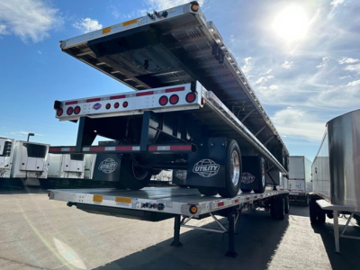 Flatbed trailer in transport position showing Utility 4000Ae branding on dual rear axles and reflective safety markings.