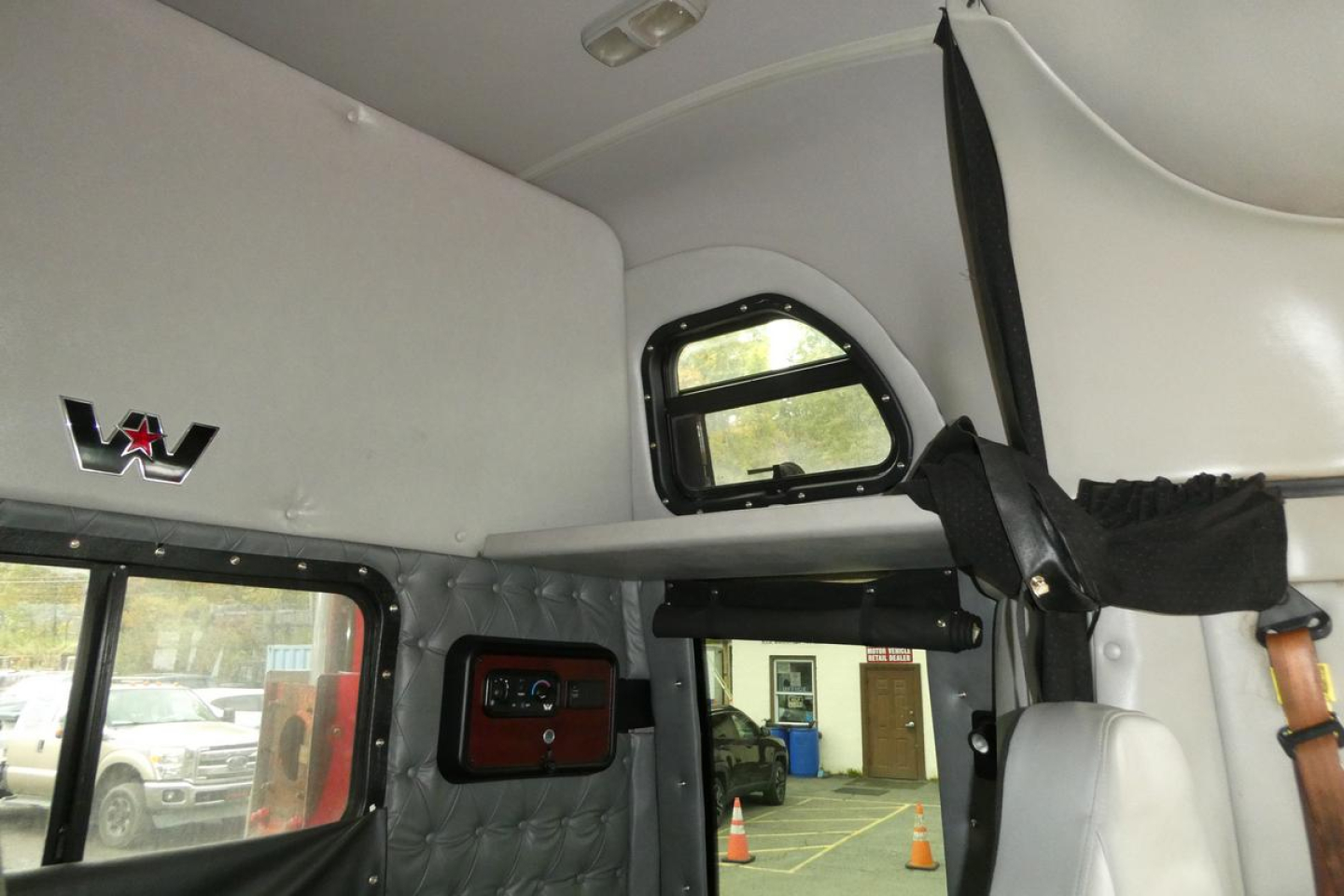 Cab interior of a Western Star 5700XE with overhead sleeper area, window, and leather quilted paneling.