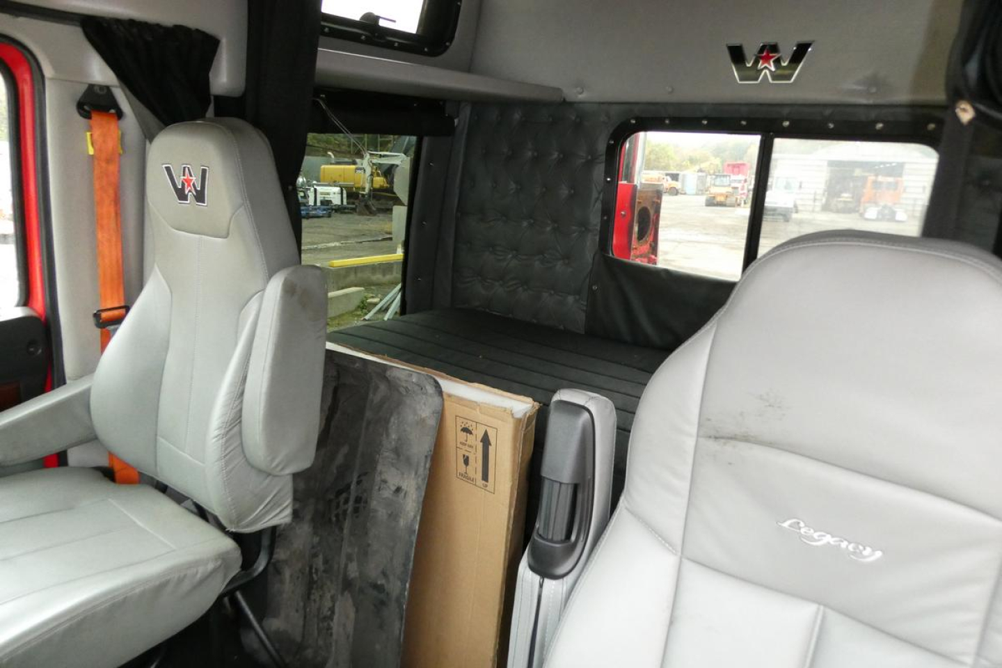 Truck cabin interior of a 2019 Western Star 5700XE showing gray seats with W emblem, partition behind, and a cardboard box between seats.