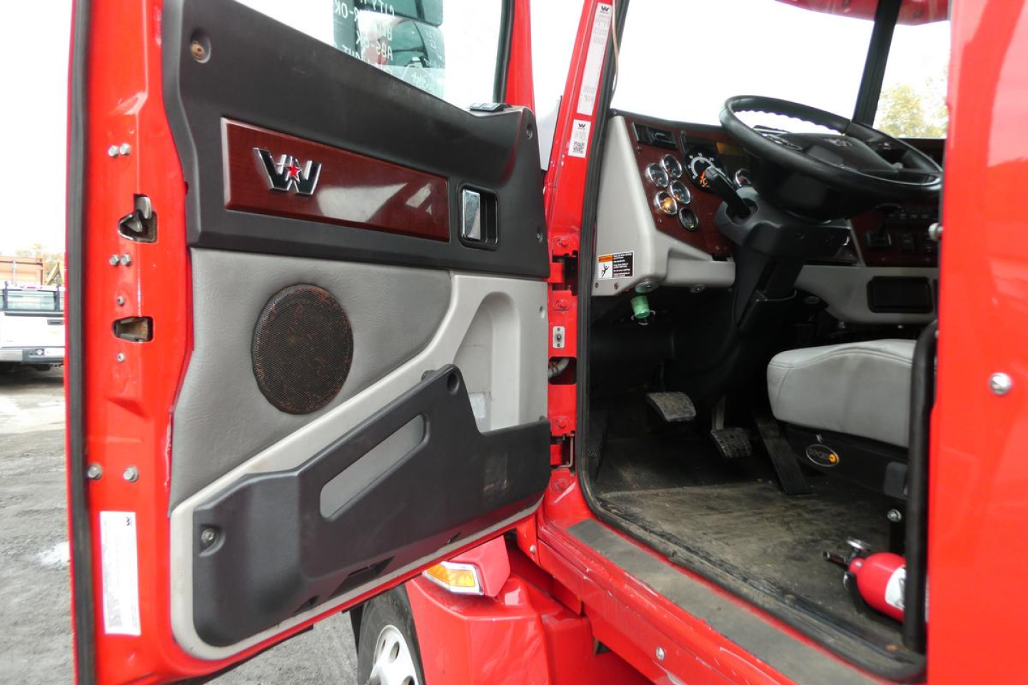 Truck cab interior showing open door and dashboard of a 2019 Western Star 5700XE with red exterior and black/gray door panel.