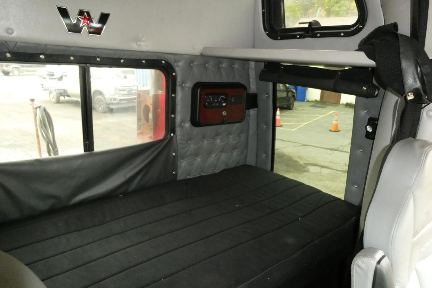 Interior sleeper cab of a 2019 Western Star 5700XE showing bunk bed area and side window with quilted paneling and storage compartment.