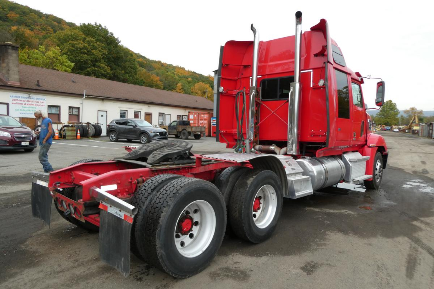 2019 Western Star 5700XE tractor with red cab, side exhaust stacks, and dual rear axles; chassis and fifth wheel area visible; outdoor lot.