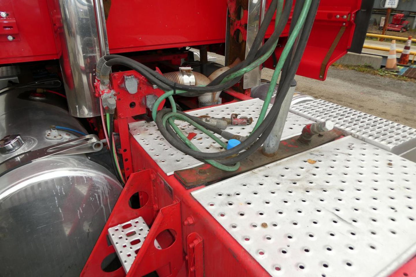 Truck battery and step area on a Western Star 5700XE, showing hydraulic lines, electrical cables, and perforated aluminum steps near the fuel tank.