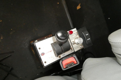 Trucks interior view showing gear shifter and control module mounted on floor beside seat, metal box with button and red lever nearby.