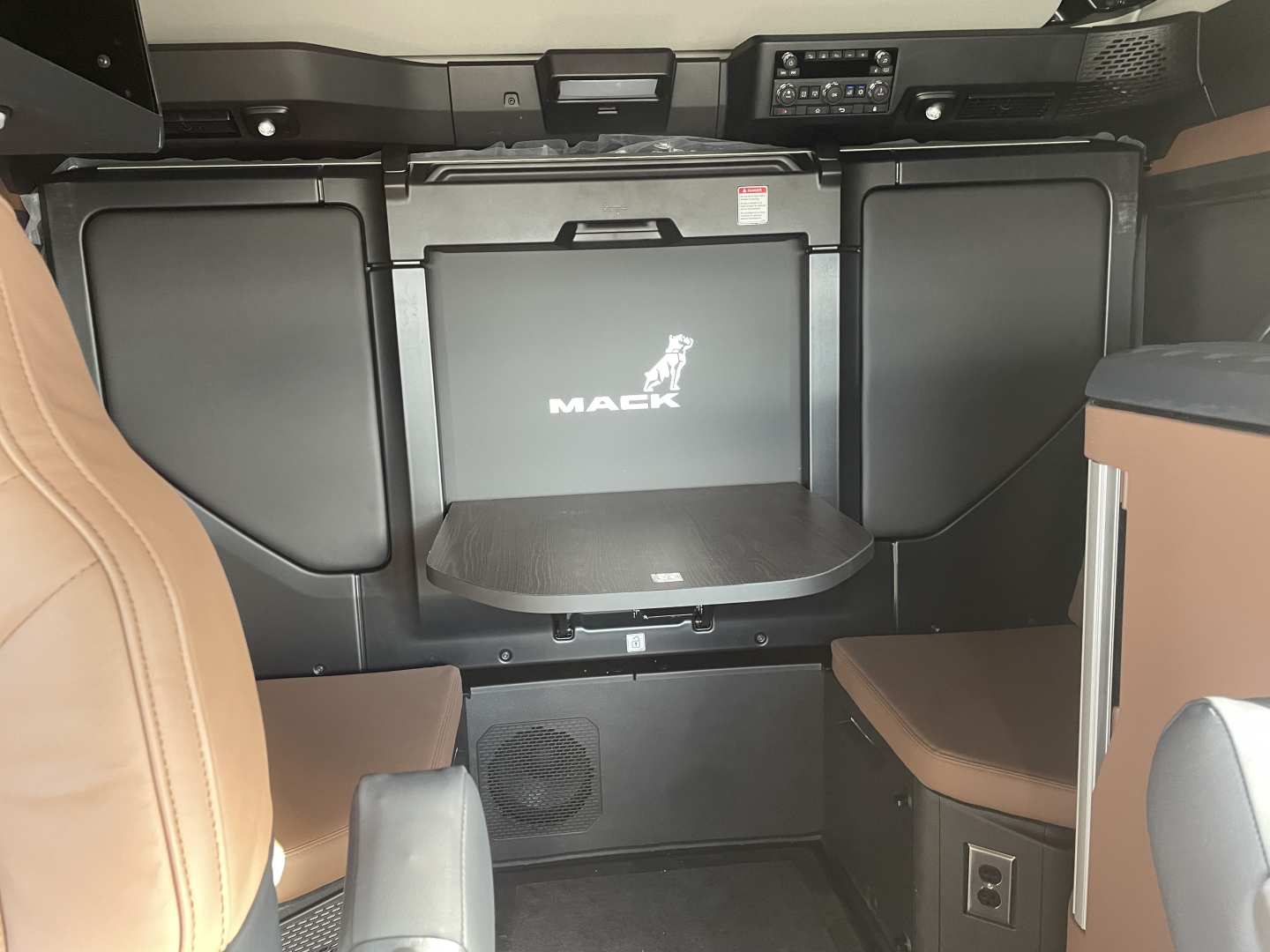 Interior of a 2026 Mack PR64T76H cab showing cargo area with seating, storage compartments, and Mack logo on center cabinet.