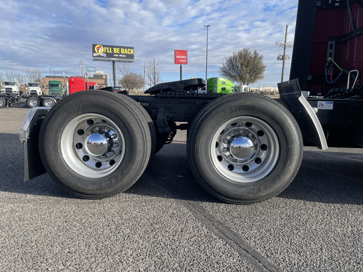 Mack PR64T76H tractor rear wheels and chassis showing two rear truck tires and polished hubcaps with fenders nearby; clear blue sky and dealership lot in background.