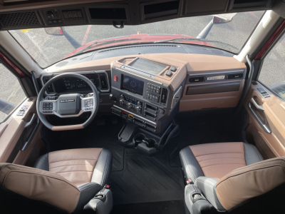 Cab interior of a new 2026 Mack PR64T76H truck showing tan and black seats, steering wheel, dashboard with control panels, gear shifter, and central console.