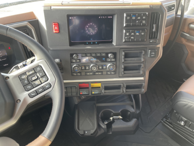 Dashboard and center console of a Mack PR64T76H truck showing steering wheel, touchscreen/instrument cluster, climate controls, switches, cup holders, and storage compartments.
