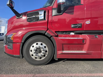 Mack PR64T76H truck side view showing front wheel, red cab, and sleeper, with chrome wheel hub and step.