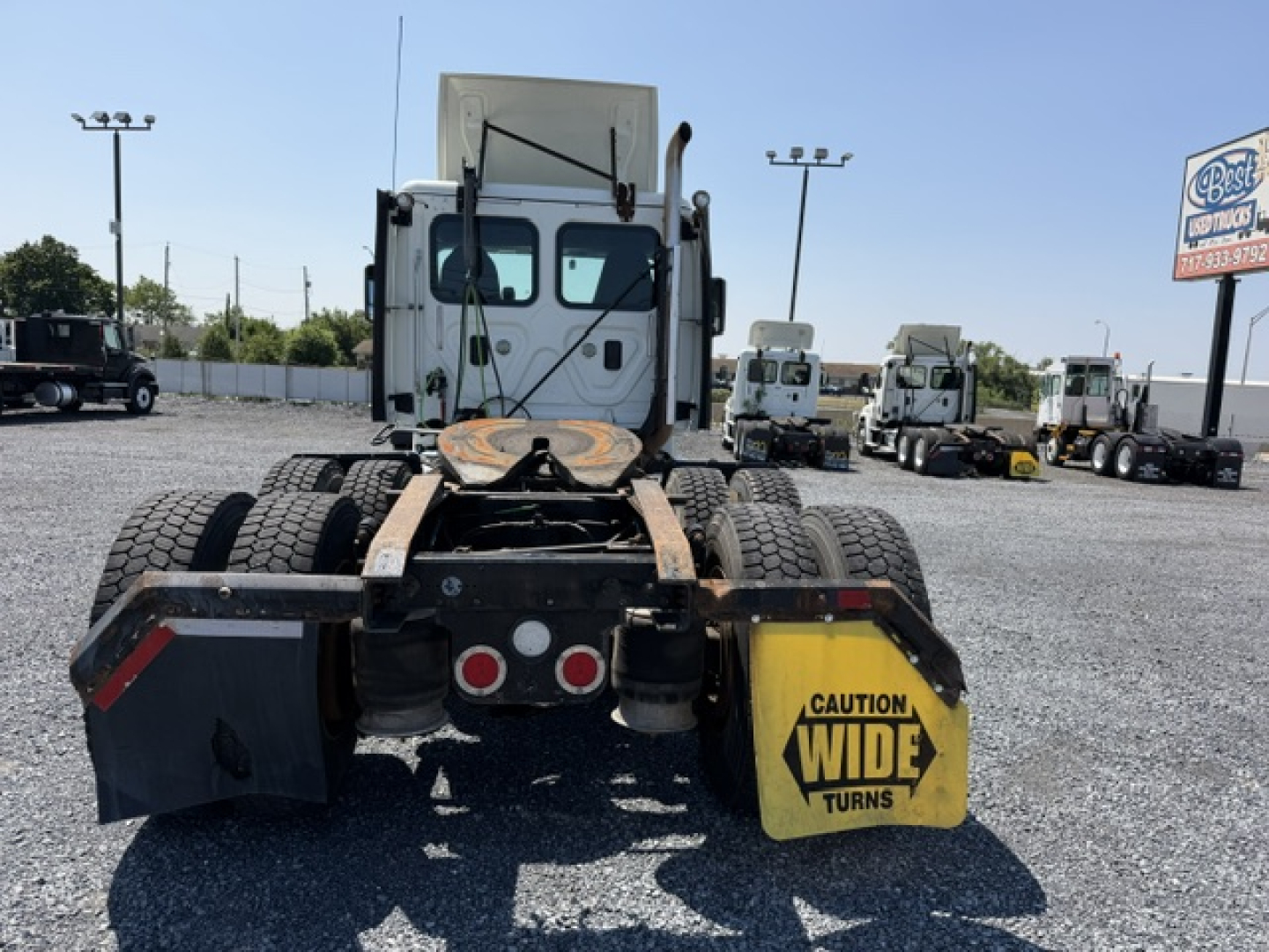 Truck rear view showing fifth wheel and dual rear axles of a 2017 Freightliner Cascadia CA125DC, with yellow caution wide turns mudflap and dual round taillights.
