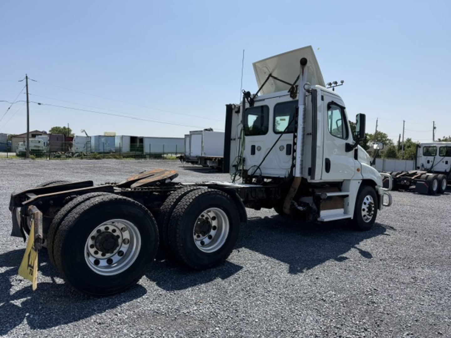 Flatbed tractor rear view showing Freightliner Cascadia CA125DC cab and dual rear axles with wheels.