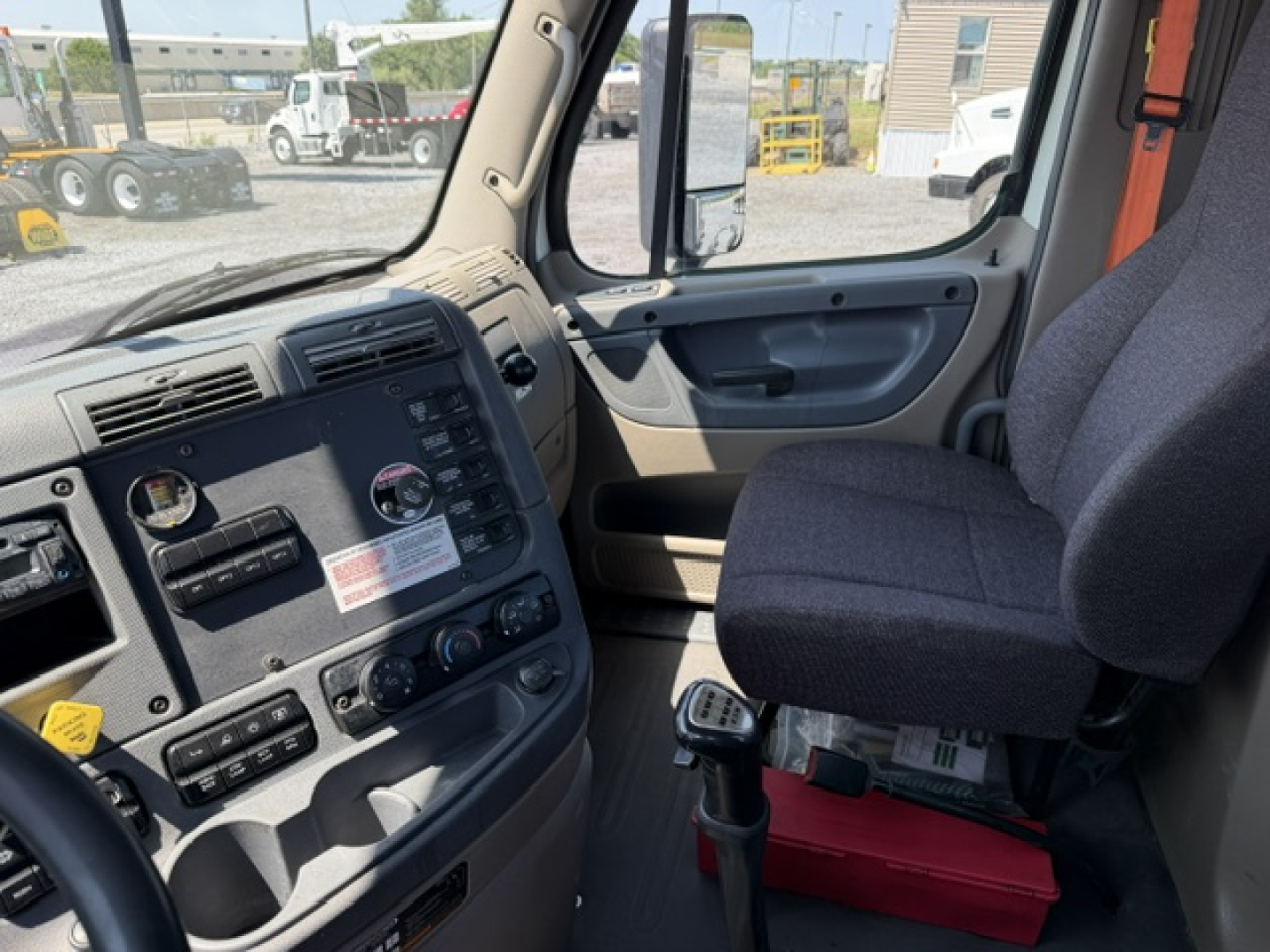 Cab interior of a Freightliner Cascadia daycab showing dashboard with gauges, steering wheel, gear shifter, and passenger seat.