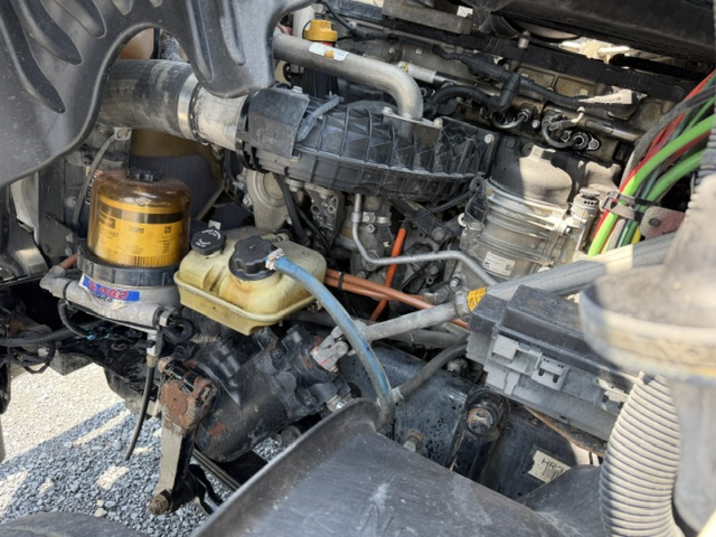 Truck engine bay showing hydraulic and coolant reservoirs, hoses, wiring, and components in a Freightliner Cascadia diesel engine area.
