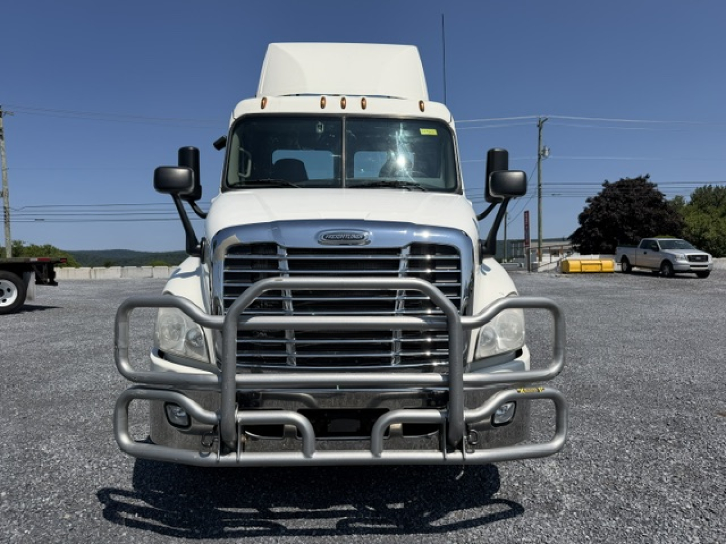 Vehicle nose of a white Freightliner Cascadia daycab showing front bumper guard and grille with large mirrors