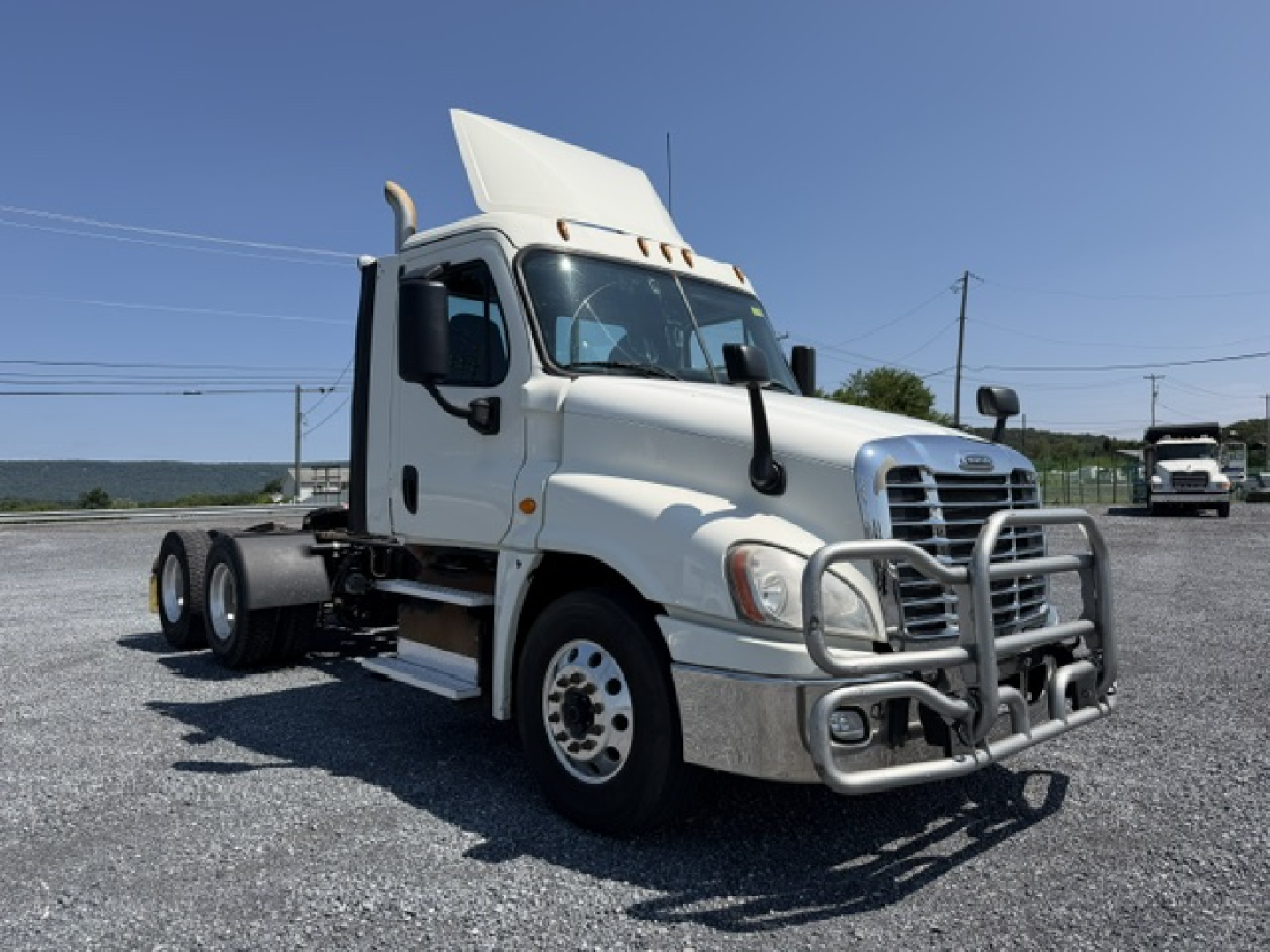 Truck front side view showing Freightliner Cascadia cab with grille guard, dual headlights, and elevated sleeper top. No visible text or labels legible on the truck itself.