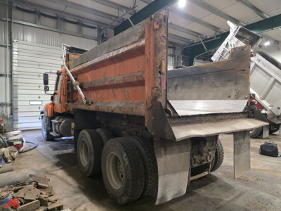 Dump truck bed of a 2019 Freightliner 114SD dump truck in a workshop, showing the orange cab and large cargo bed with side walls and rear tailgate.