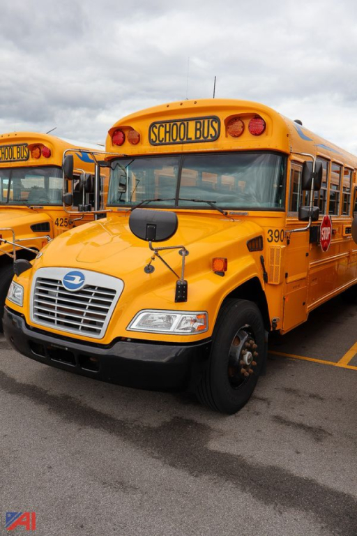School bus front view showing bright yellow body, blue Bird emblem on grille, 'SCHOOL BUS' sign above windshield, and orange warning lights.