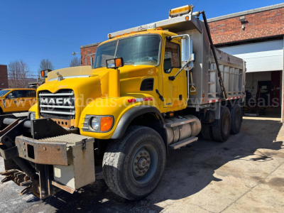Mack CV713 dump truck in yellow with front bumper attachment and dump bed, side view showing wheel, cab, and crane light bar.