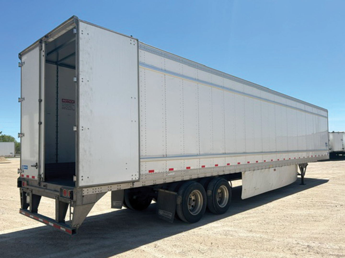 Trailer end showing open rear door and tandem axle configuration with silver aluminum sides.
