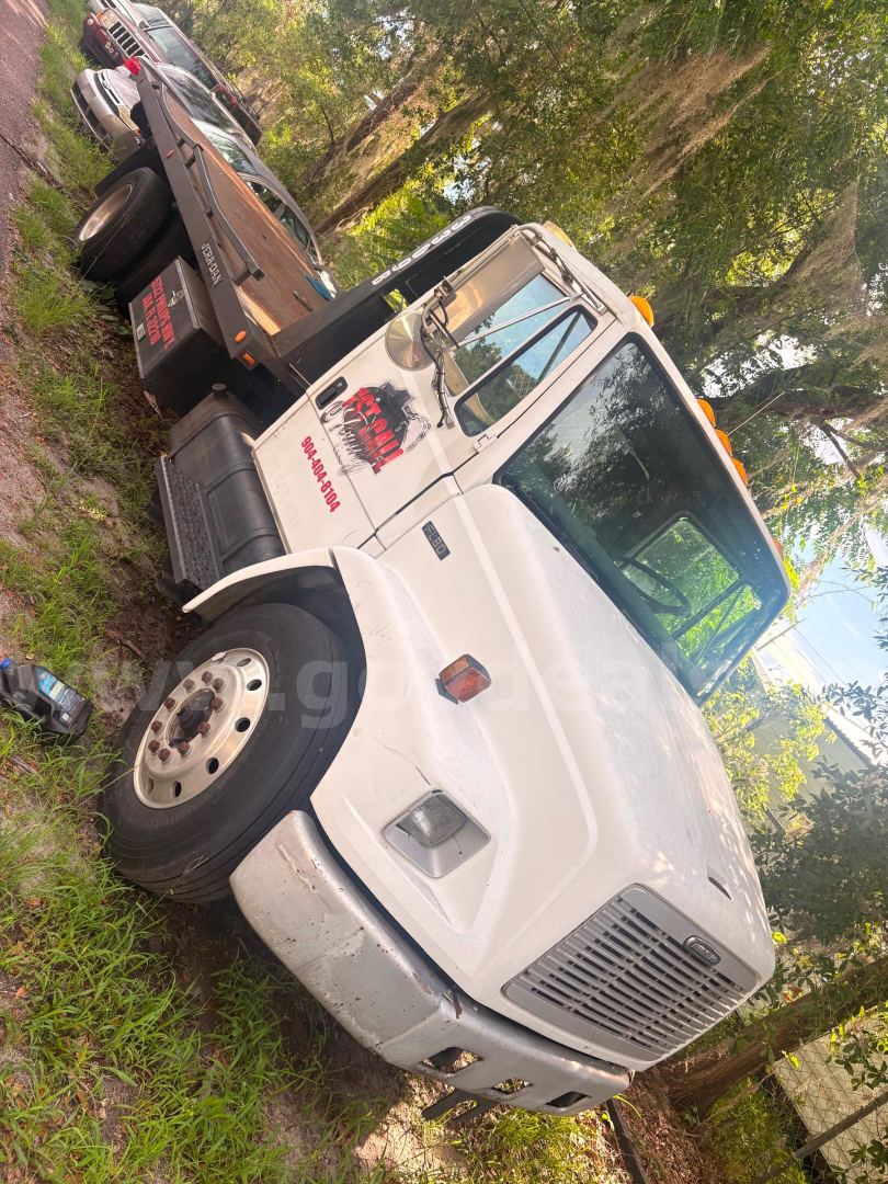 Freightliner FL80 tow truck cab front view showing white body and crew cab with logo on door.