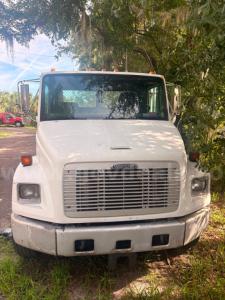 Front view of a white 2003 Freightliner FL80 tow truck showing large grille, bumper, headlights, and windshield with side mirrors.