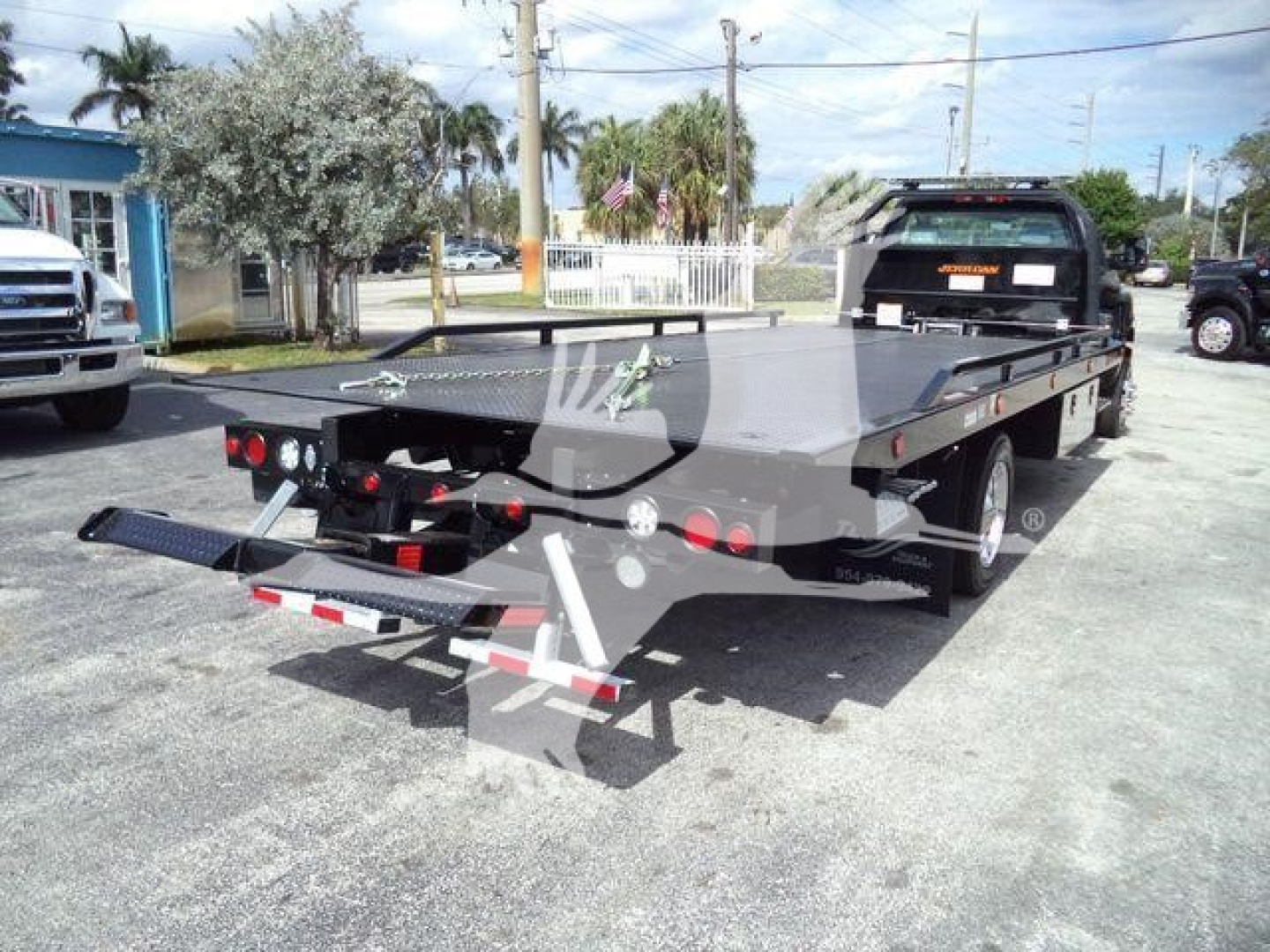 Flatbed rollback tow truck rear view showing a black heavy-duty car carrier with metal headache rack and multiple tail lights; 2023 International CV listing details visible.