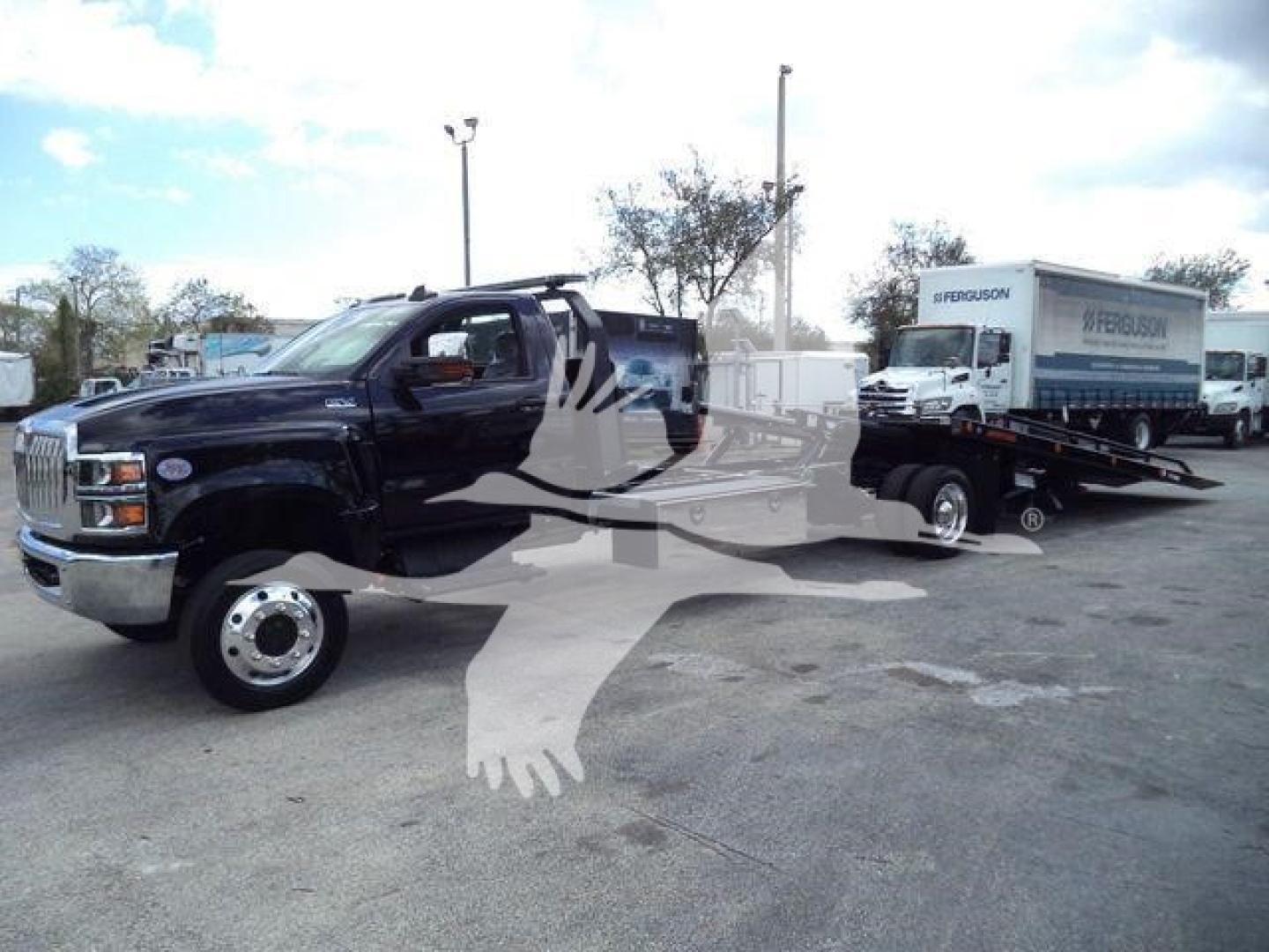 Black rollback tow truck with a medium-duty cab and a white Spectre Towing flatbed trailer in a dealership lot. Visible text on the trailer reads WRETFUSION? or generic. The front chrome bumper and wheel, with background trucks and a cloudy