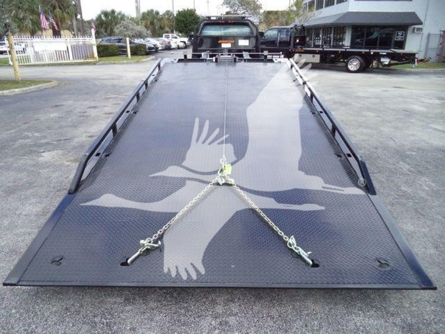 Flatbed tow truck cruiser showing a black metal rollback bed with chains and hooks on the deck, International CV rear view.