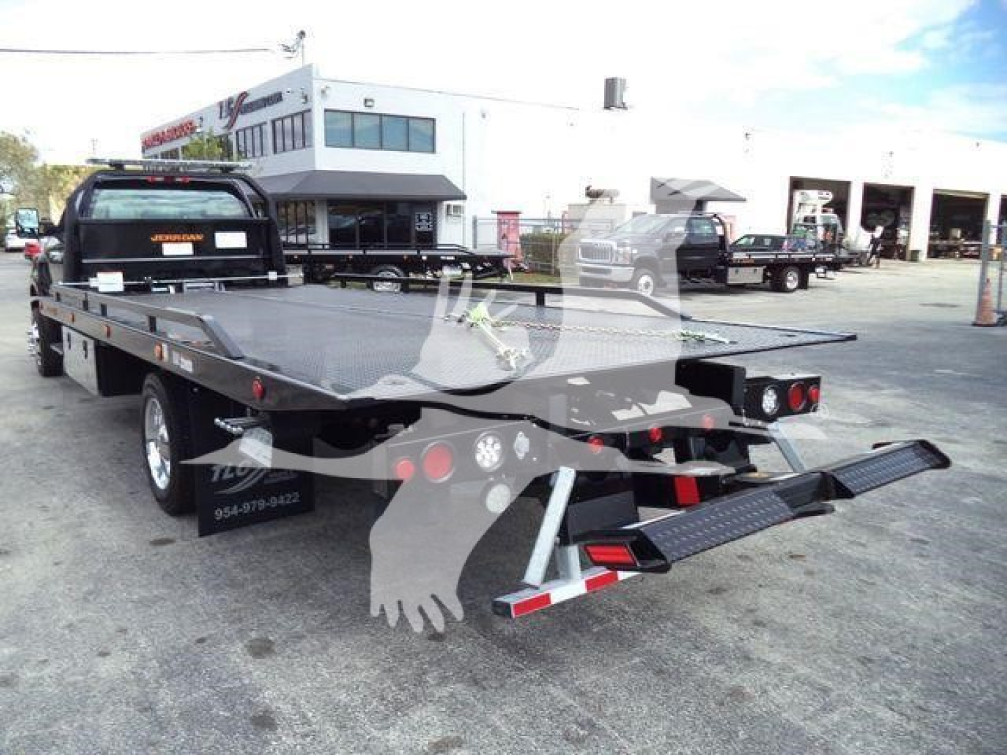 Truck rollback flatbed showing rear view with folded ramps and taillights; license plate area not visible; dealership background.