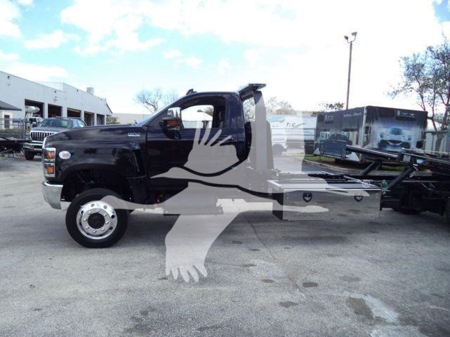Black International CV rollback truck side view with a large white overlay of a bird logo across the image. The cab area shows standard truck features with a long flatbed and wheel well. No legible alphanumeric labels or text visible on com