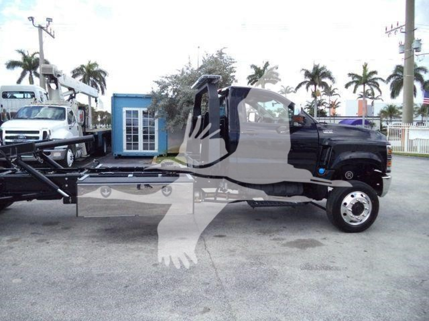 Truck cab and rollback wrecker chassis visible with extended flatbed and wheel; VIN plate and stock number not legible; palm trees in background.