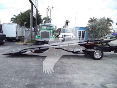 Flatbed tow truck with extended ramp in a lot, International CV image with other trucks in background.