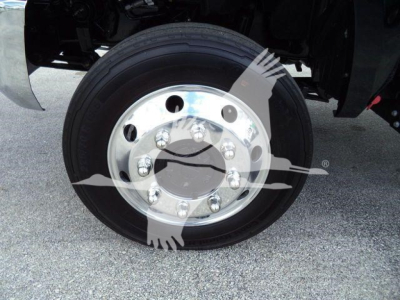 Truck wheel with silver hubcap and black tire; shows front right wheel and part of suspension under a 2023 International CV rollout truck.