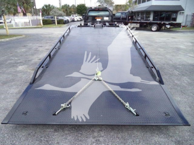Flatbed tow truck cruiser showing a black metal rollback bed with chains and hooks on the deck, International CV rear view.