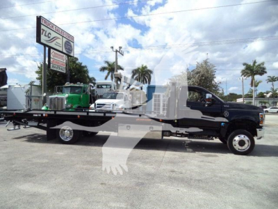 Flatbed tow truck from side view showing International CV chassis, long lowbed with dual rear wheels, and signage in background.