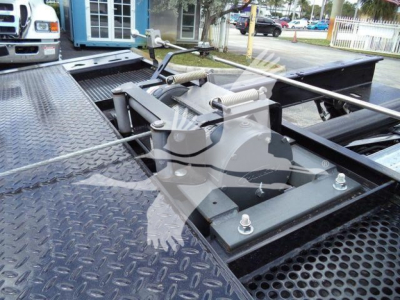 Truck bed with hydraulic rollover hoist mechanism and tie-down hardware in the center of a black diamond-plate platform.