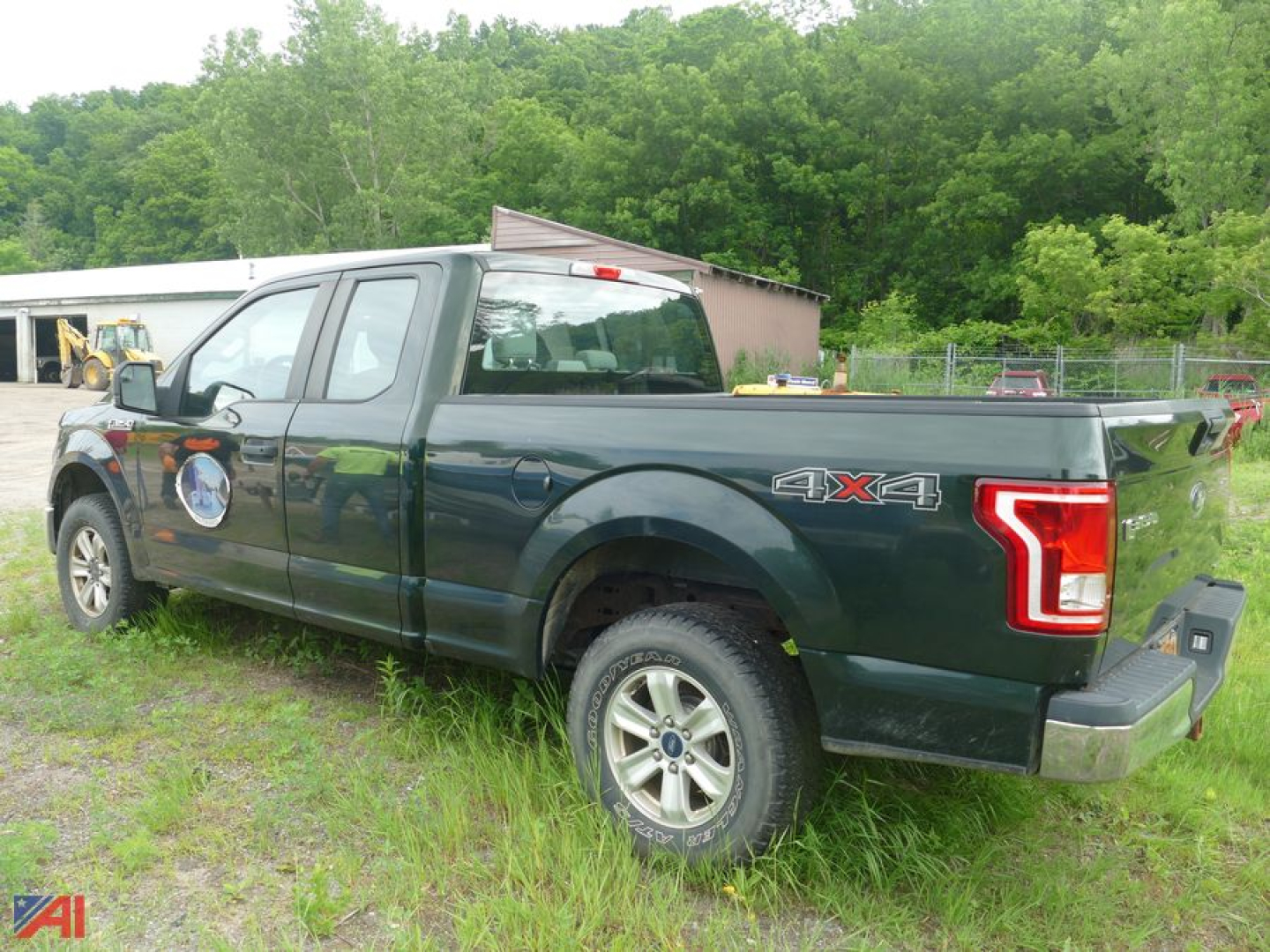 Ford F-150 pickup truck with 4x4 badge on rear-side, dark green color, extended cab, in grassy lot.