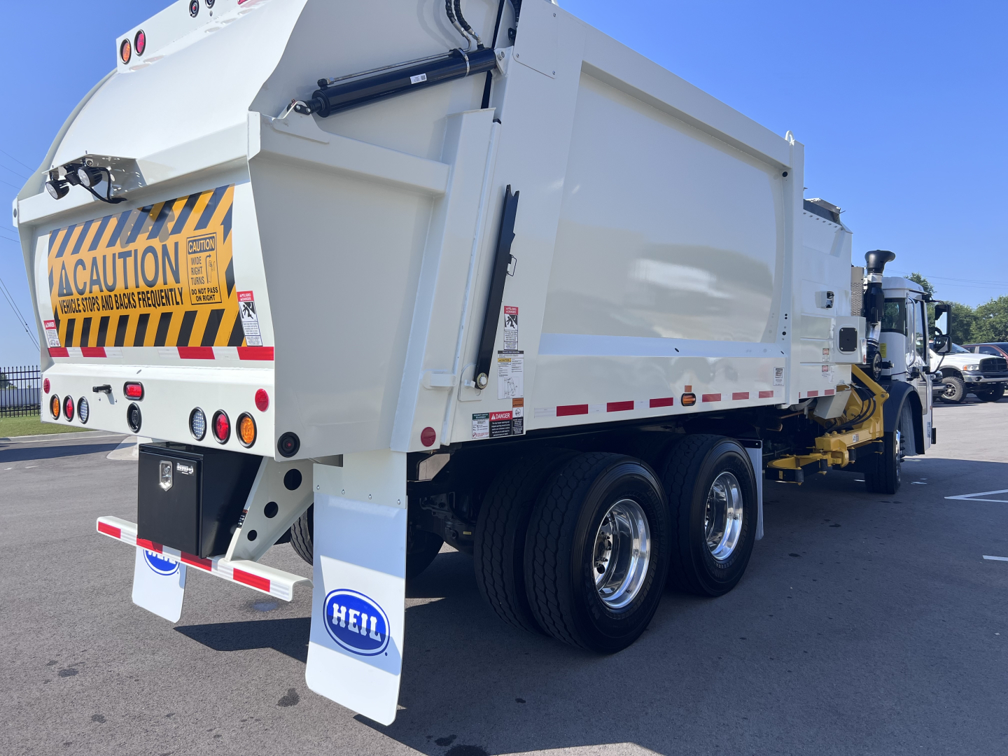 Rear three-quarter view of a white Mack LR64 dump truck body showing dual rear axles, caution decal, and HEIL mudflaps.