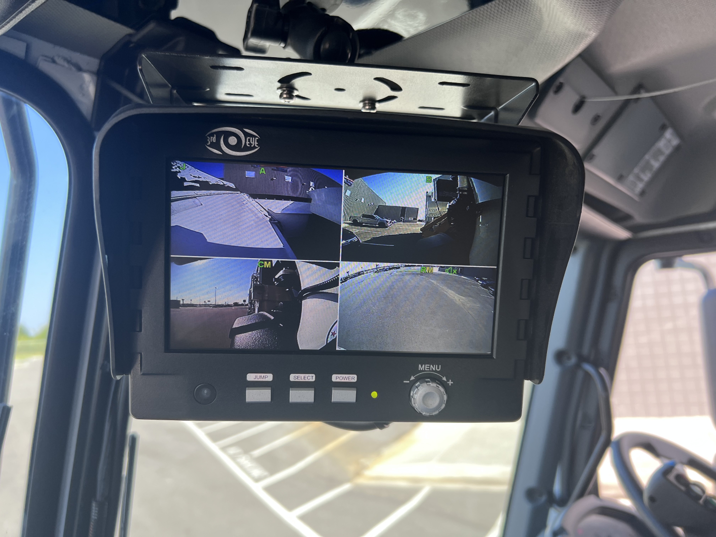 HD monitor mounted in Mack LR64 cab showing four camera feeds: front, left, right, and rear views; small control buttons below screen.