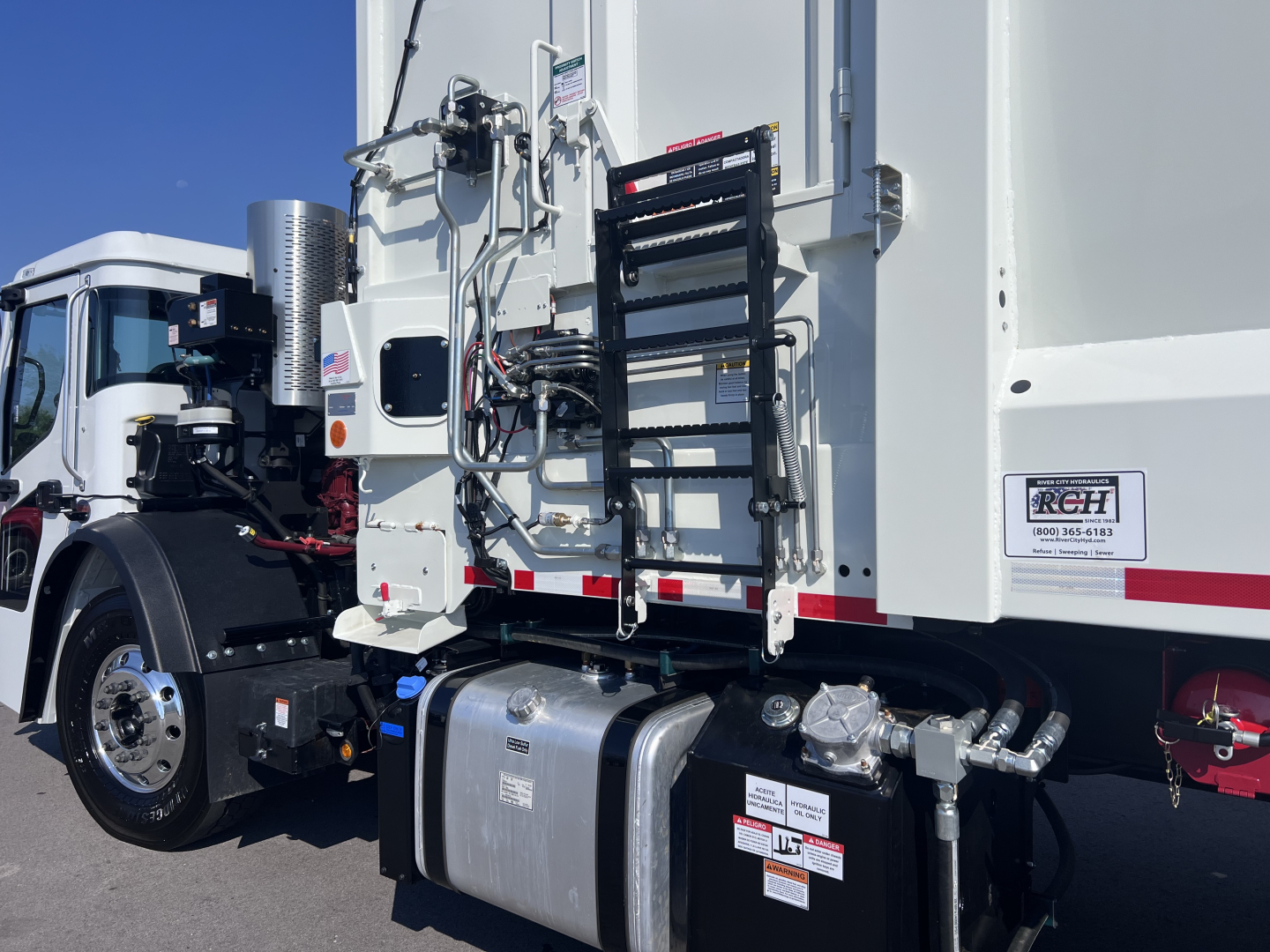 Mack LR64 dump truck rear/side view showing fuel tank, ladder, hydraulic lines, and chassis components with VIN sticker.
