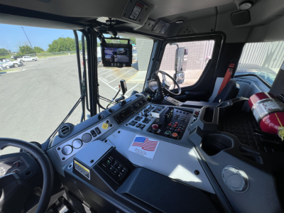 Dashboard and steering wheel of a new Mack LR64 truck cab showing control panels, gauges, and a fire extinguisher mounted to the right.