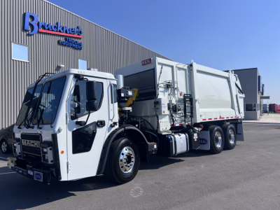 Mack LR64 cab-over-engine garbage truck showing white body and gray rear dump body, front grille with Mack logo, side view with cargo bed and hydraulic system.