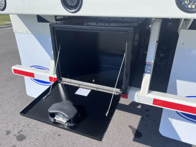 Rear of a 2026 Mack LR64 dump truck showing a lowered toolbox and latch with a small receptacle inside the open compartment.