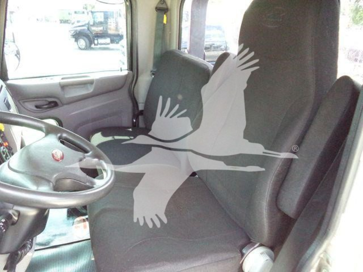 Truck cab interior with steering wheel and driver's seat visible, watermark of a flying bird overlay covers center; no legible labels or serials visible.