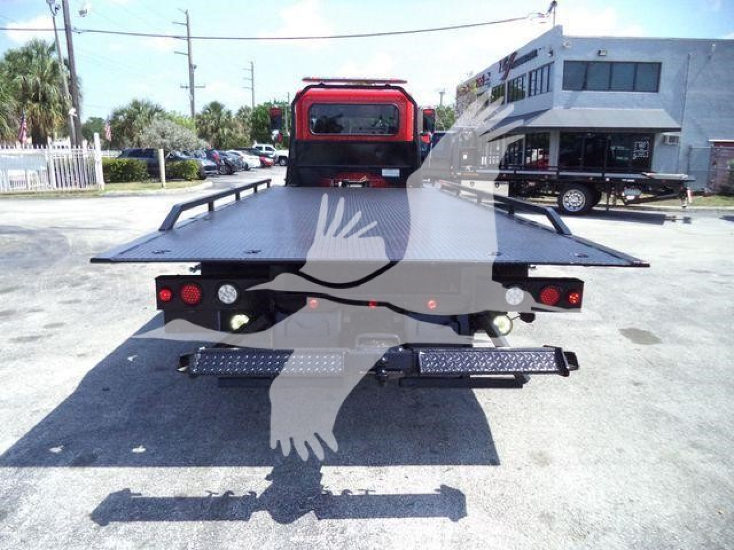Rear view of a flatbed tow truck with loading platform extended, red cab, and dual rear LED lights.