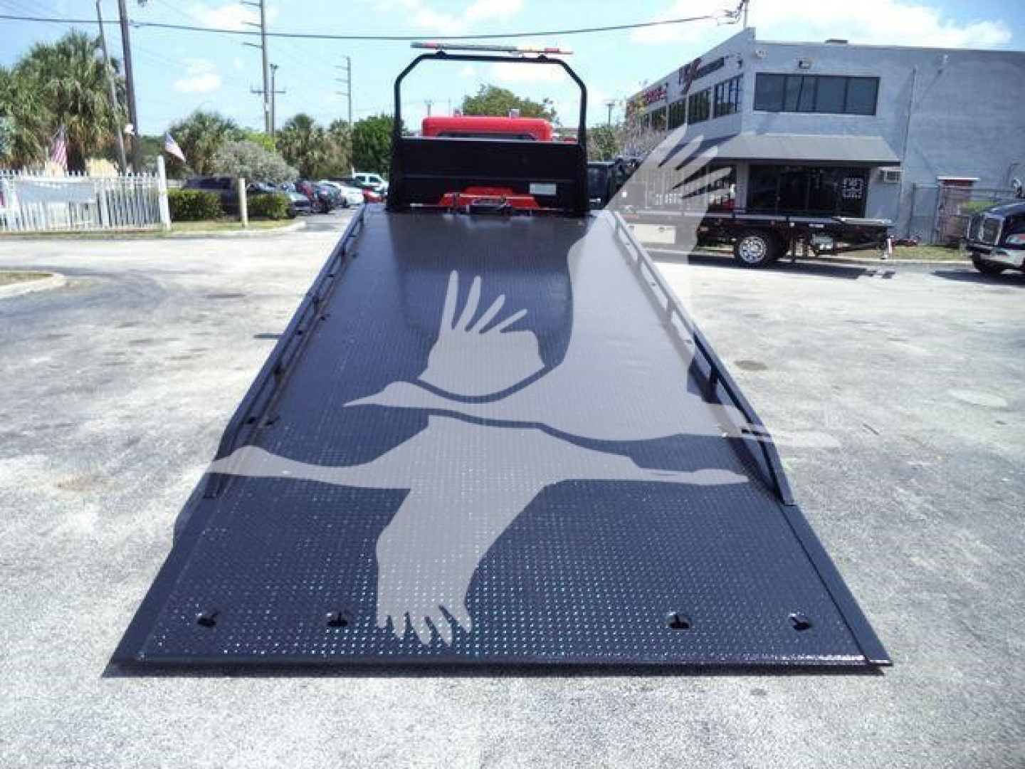 Peterbilt 337 rollback truck with a flatbed ramp and white bird logo on the metal surface, showing the rear platform and surrounding lot.