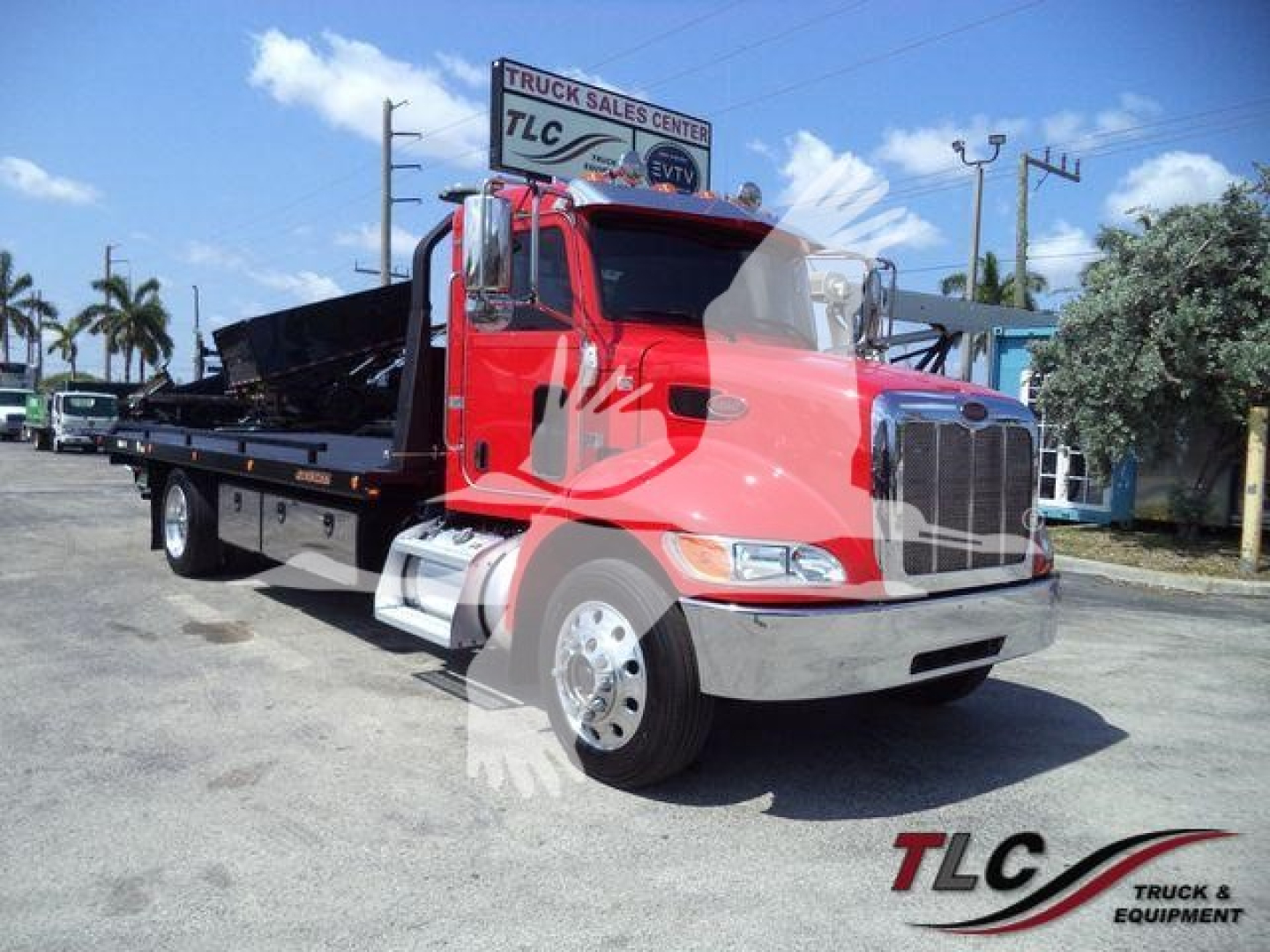 Peterbilt 337 rollback truck in red with flatbed and chrome front, cab view, parked at dealer lot.