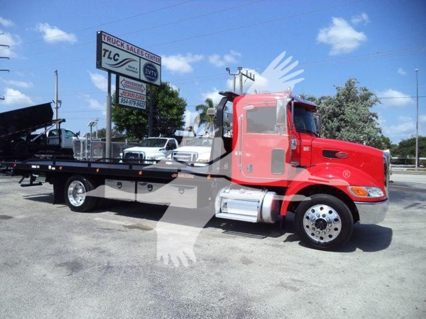 Peterbilt 337 rollback truck in red cab with flatbed in a dealership lot. Visible text includes TLC Truck Sales Center sign and truck details on the lot.